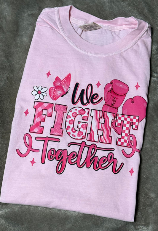 Pink t-shirt with 'We Fight Together' text and boxing glove graphics on a gray surface